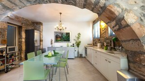 A modern kitchen with a stone arch, a glass dining table, green chairs, and a hanging light fixture. - Muazzo Creta Stone House, Nature Escape with Pool (Rethymno)