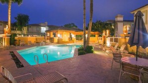 A swimming pool with lounge chairs and umbrellas, surrounded by buildings with warm lighting. - Relax Poolside in your private, Clean, Beautiful, Quiet Vacation Condo (Phoenix)