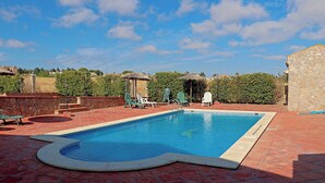 Ein rechteckiger Pool mit gefliestem Rand, umgeben von roten Fliesen und grünen Stühlen.