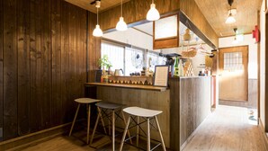A wooden interior with a bar area, stools, and hanging lights. - Guest House Maru ‐Hostel (Kashima)