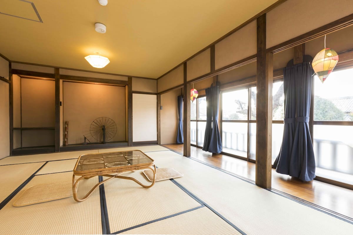 A traditional Japanese room with tatami flooring, a low table, sliding doors, and a view of a mountainous landscape.