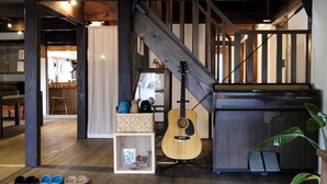A wooden staircase with a guitar leaning against a wall, a shoe rack with various slippers, and a small shelf with decorative items. - Guest House Maru ‐Hostel (Kashima)