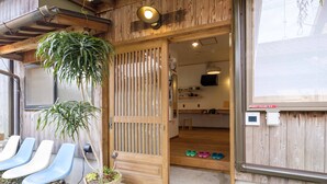 A wooden exterior with a sliding door, a potted plant, and a row of blue chairs outside. - Guest House Maru ‐Hostel (Kashima)