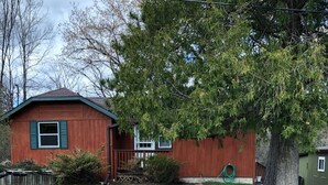Une maison en bois d’un seul étage, avec un toit rouge, un porche à l’avant et une pelouse verte.