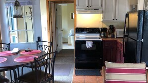 Une cuisine compacte équipée d’une cuisinière, d’un réfrigérateur et de meubles blancs. On y trouve un coin repas avec une table et des chaises, ainsi qu’une fenêtre donnant sur un paysage agréable.