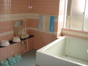 A bathroom with a bathtub, a shower, and a sink. There are toiletries on the counter and a towel hanging on the wall. - Cabin KUMAGAYA (Kumagaya)