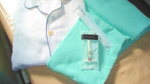Una camisa blanca doblada con cuello y botones, una toalla color turquesa, y un pequeño paquete con la etiqueta 'FINE QUALITY'.