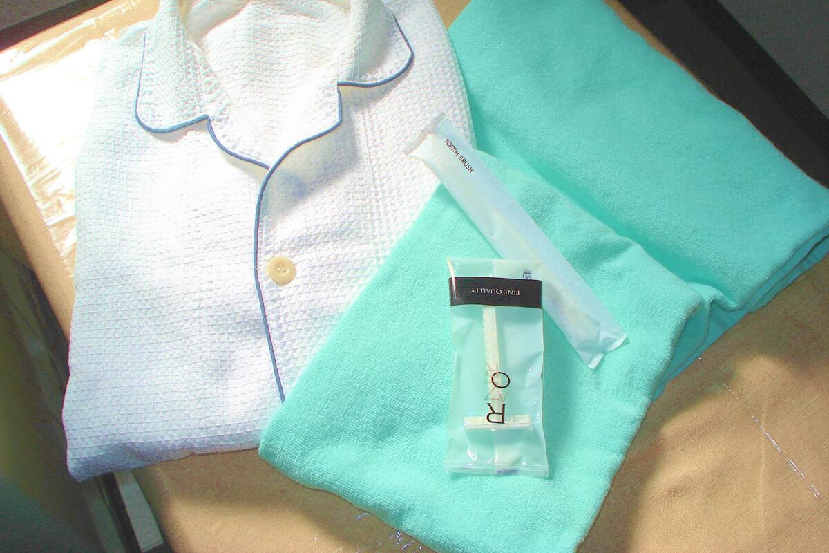 Una camisa blanca doblada con cuello y botones, una toalla color turquesa, y un pequeño paquete con la etiqueta 'FINE QUALITY'.