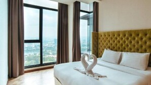 Hotellihuone, jossa on suuri sänky, vihreä, napitettu pääty ja suuret ikkunat, joista avautuu näkymä kaupungin siluettiin.
