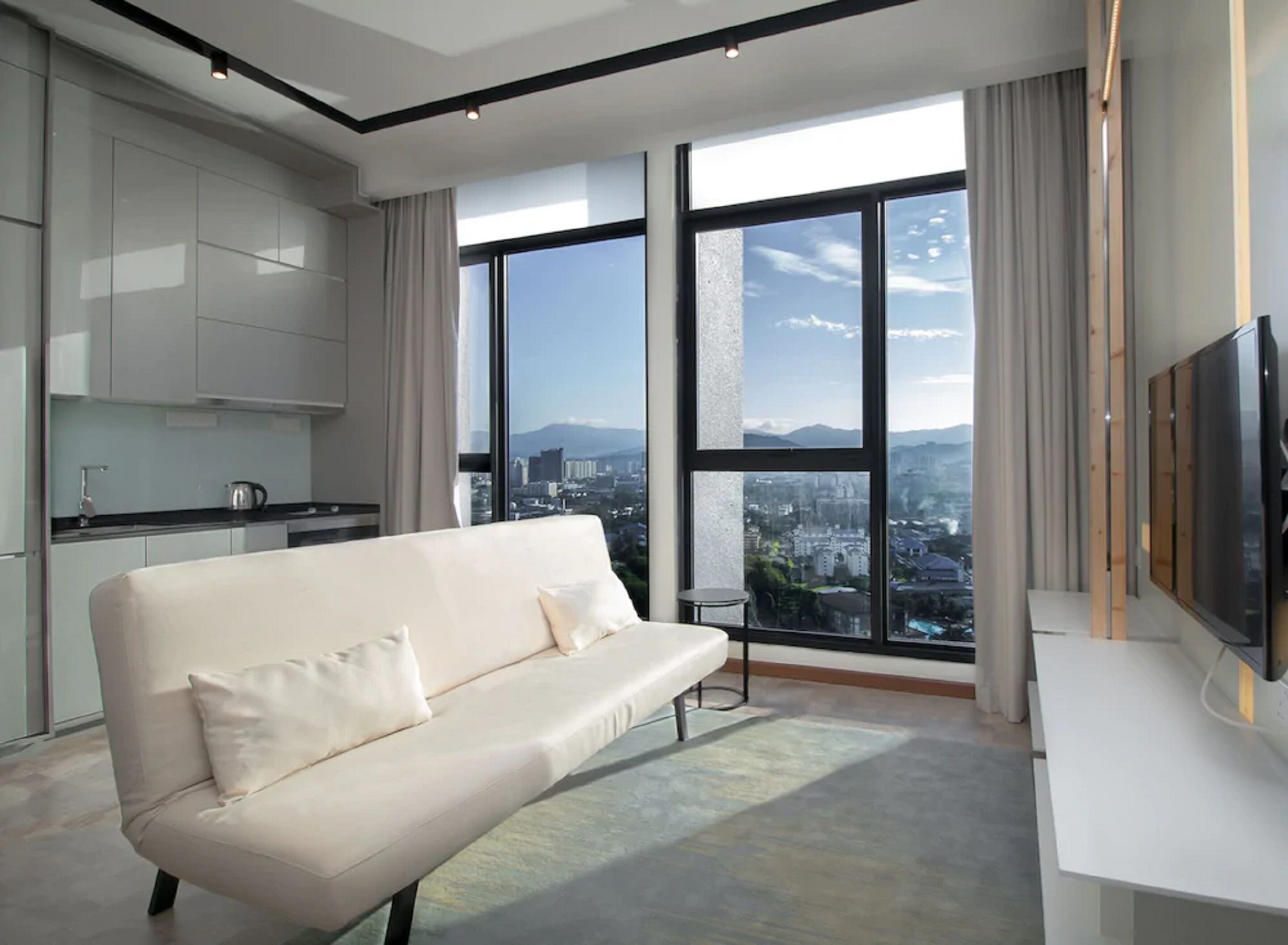 A modern living room with a sofa, a TV, and large windows offering a city view.