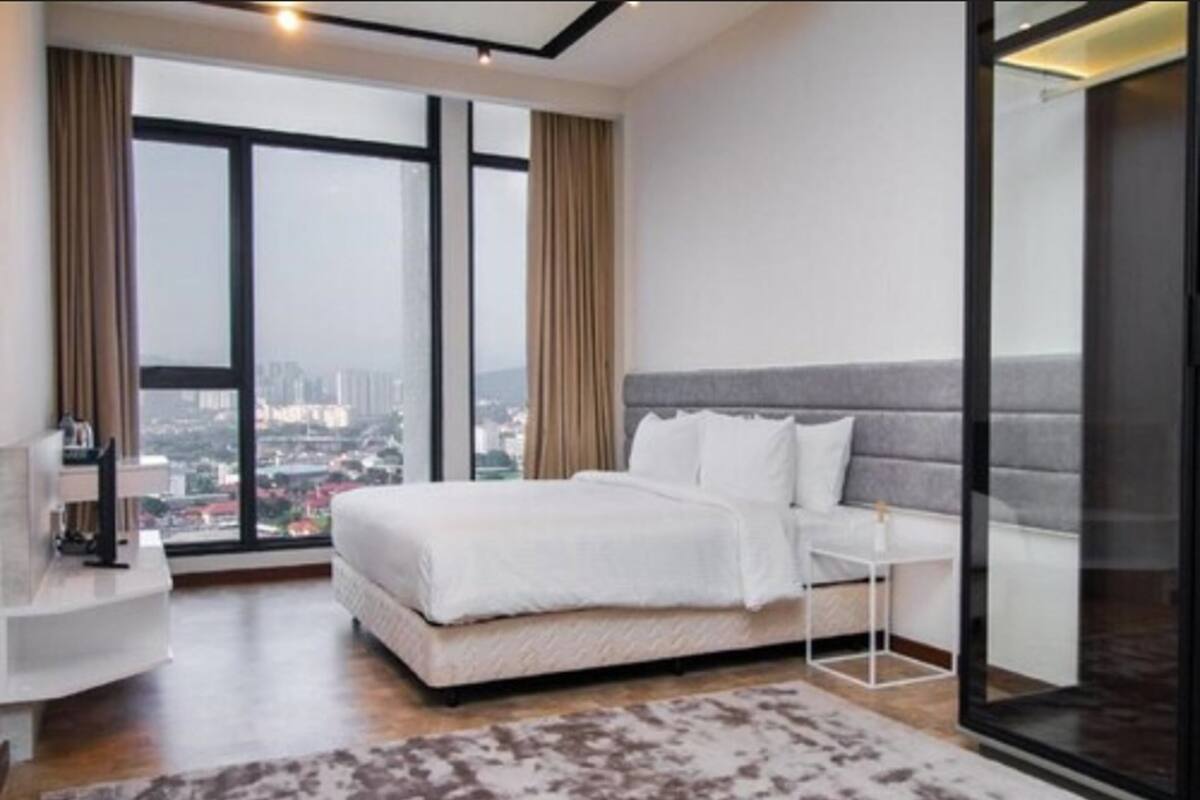 A modern bedroom with a large window, a bed, a bedside table, and a view of the city.