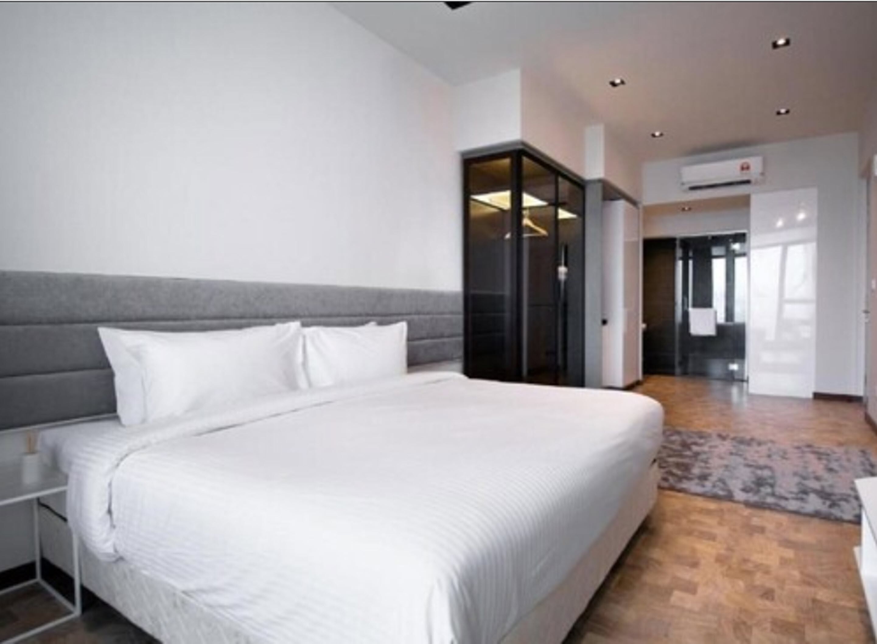 Une chambre d’hôtel moderne avec un grand lit, une tête de lit grise et un dressing.