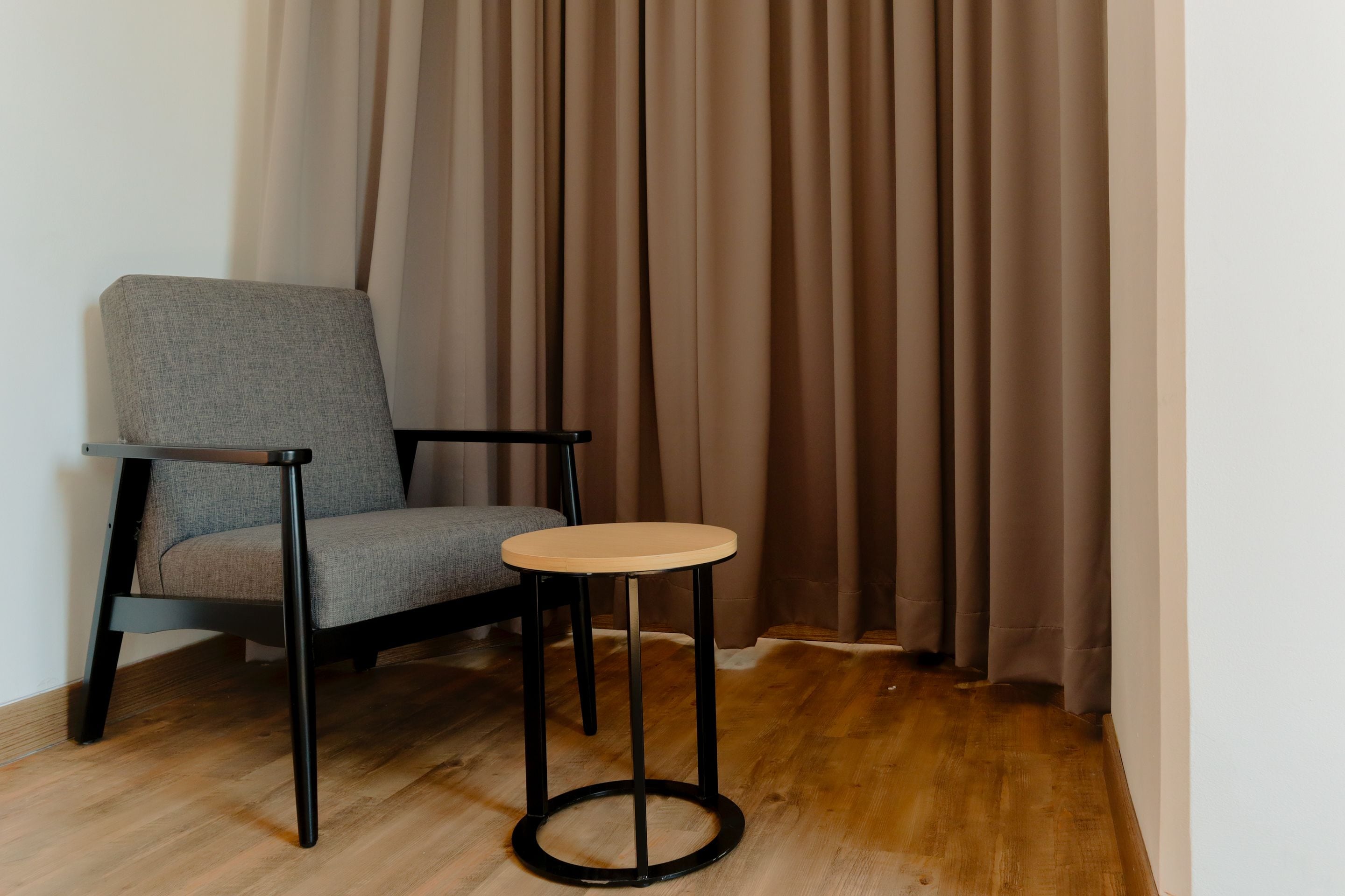 A chair and a small round table in a room with wooden flooring and curtains.