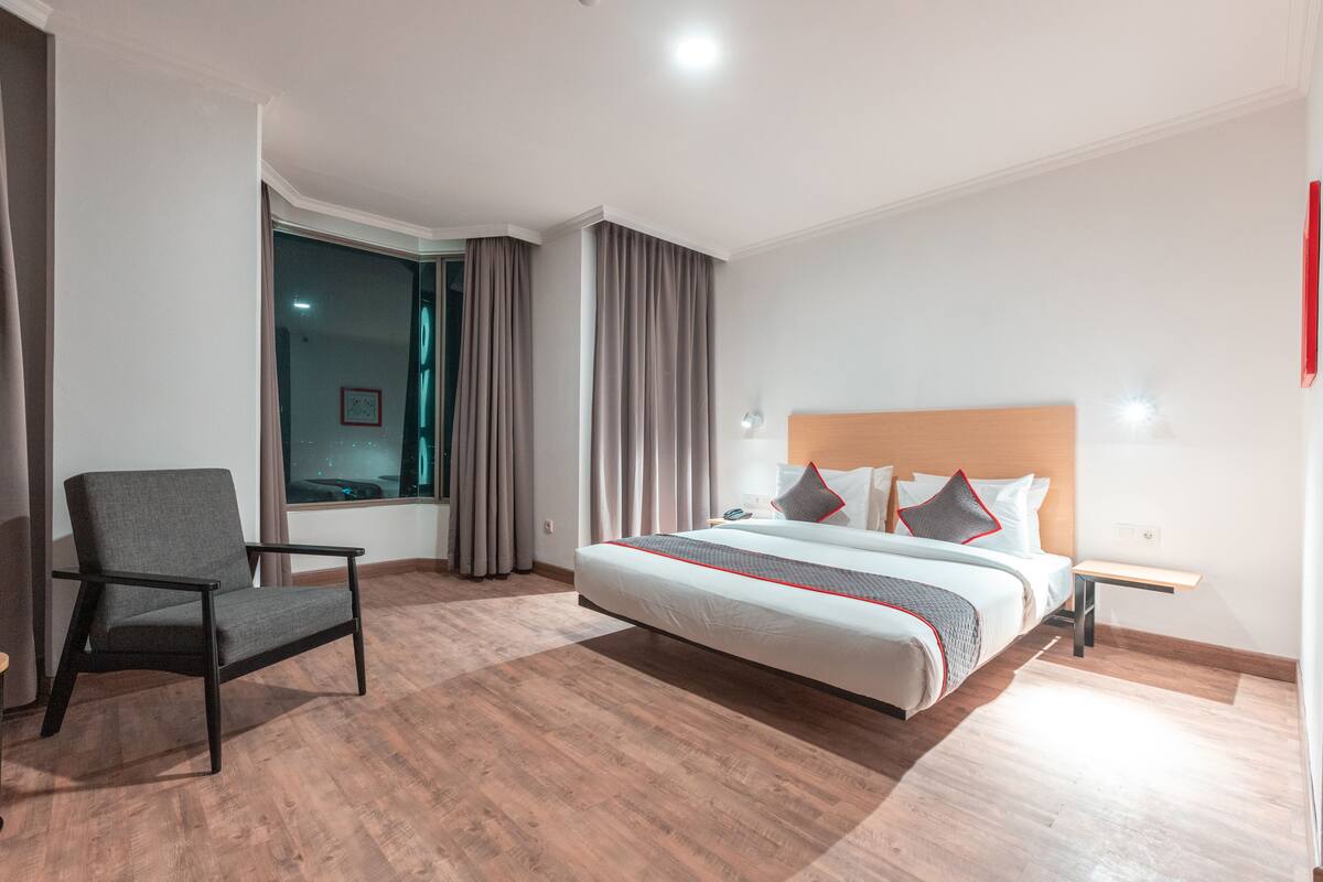 Une chambre d’hôtel moderne avec un grand lit, une chaise, une table de chevet et une fenêtre avec des rideaux.