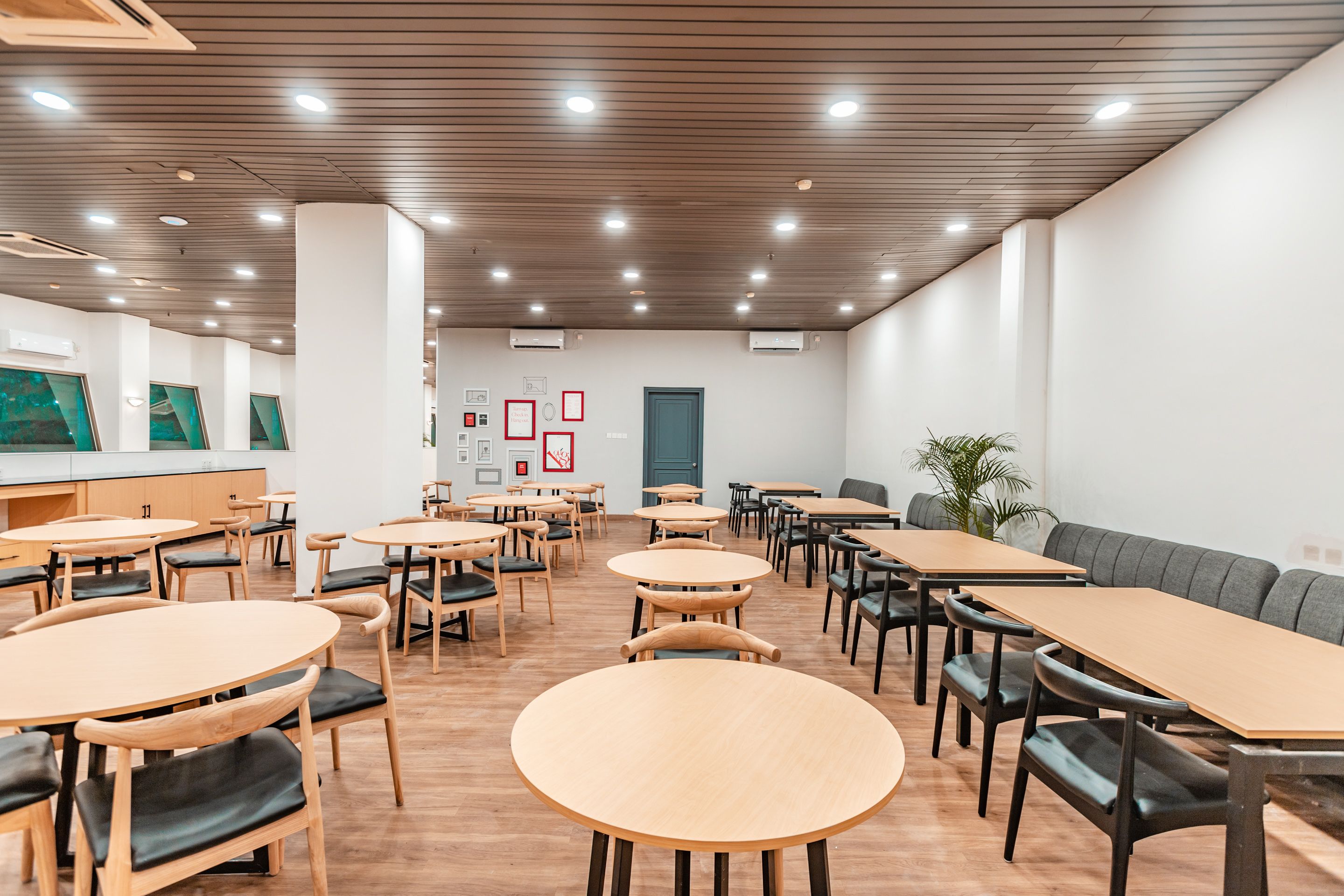 A spacious dining area with round and rectangular tables, wooden flooring, and a modern ceiling design.