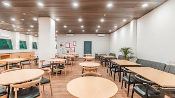 A spacious dining area with round and rectangular tables, wooden flooring, and a modern ceiling design.
