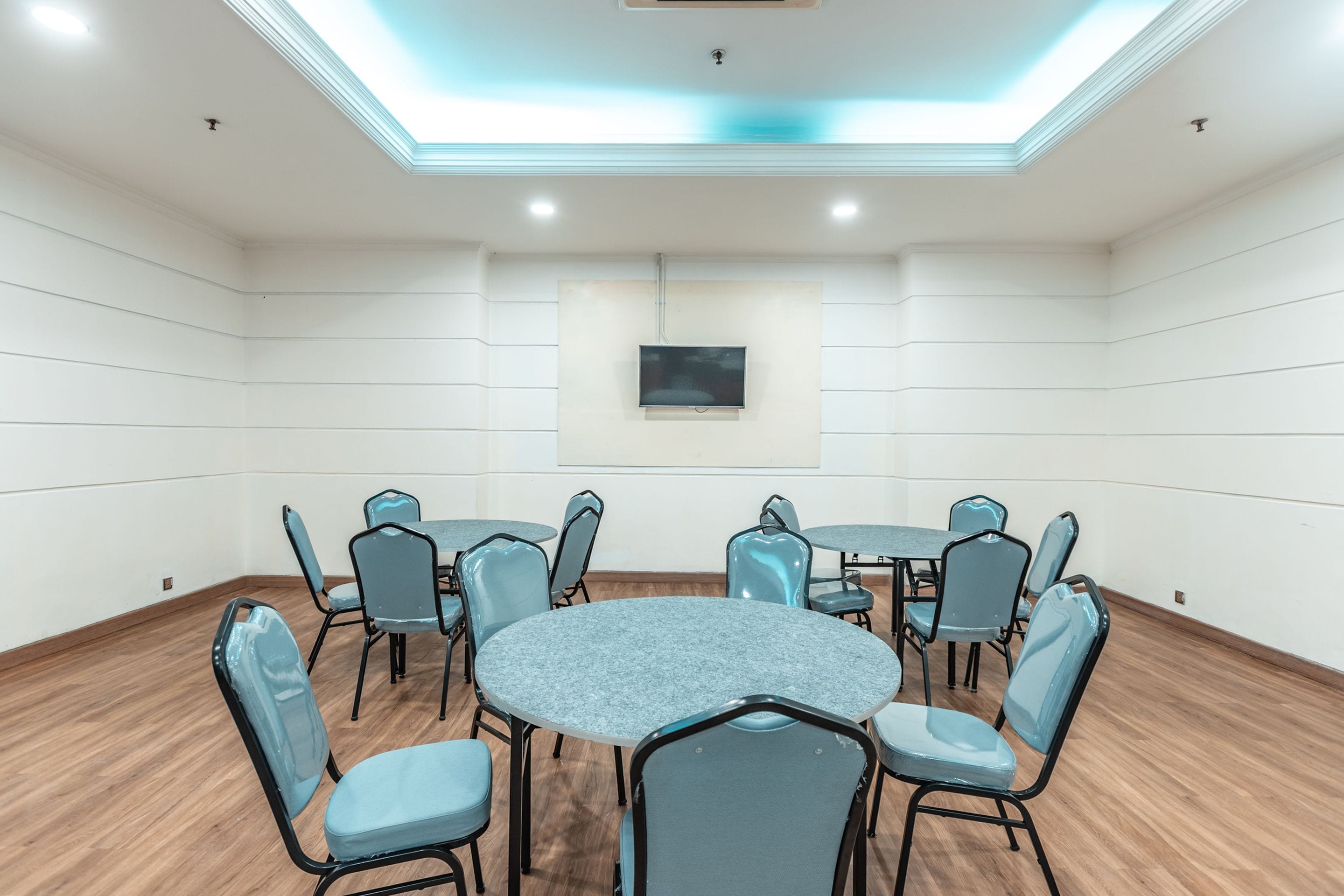 A conference room with a round table, six chairs, a flat-screen TV, and a ceiling light fixture.