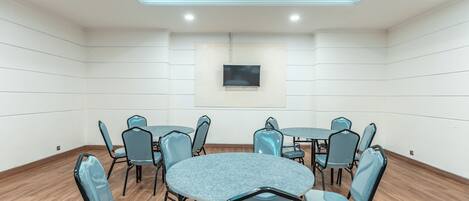 A conference room with a round table, six chairs, a flat-screen TV, and a ceiling light fixture.
