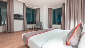 A modern hotel room with a large bed, a chair, a TV, and large windows with curtains. - Super OYO Townhouse 2 Hotel Gunung Sahari (Jakarta)