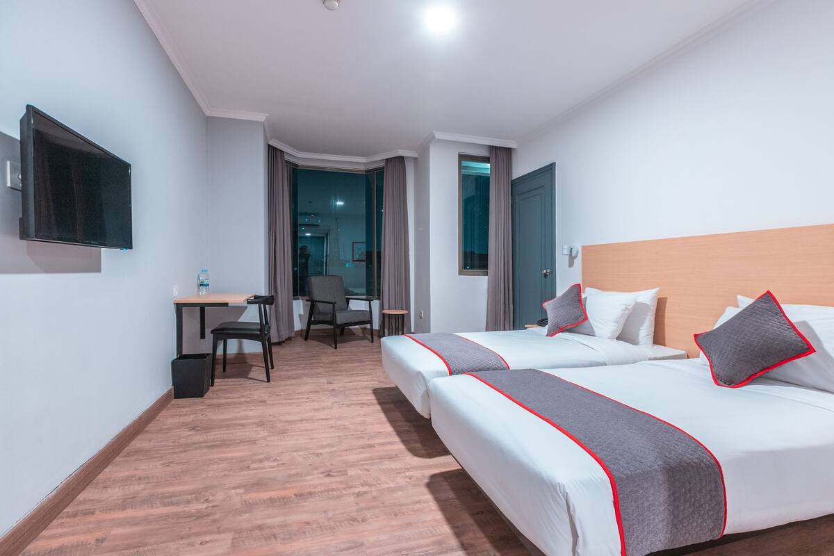 Une chambre d’hôtel avec deux lits, un bureau, une chaise et un téléviseur fixé au mur.