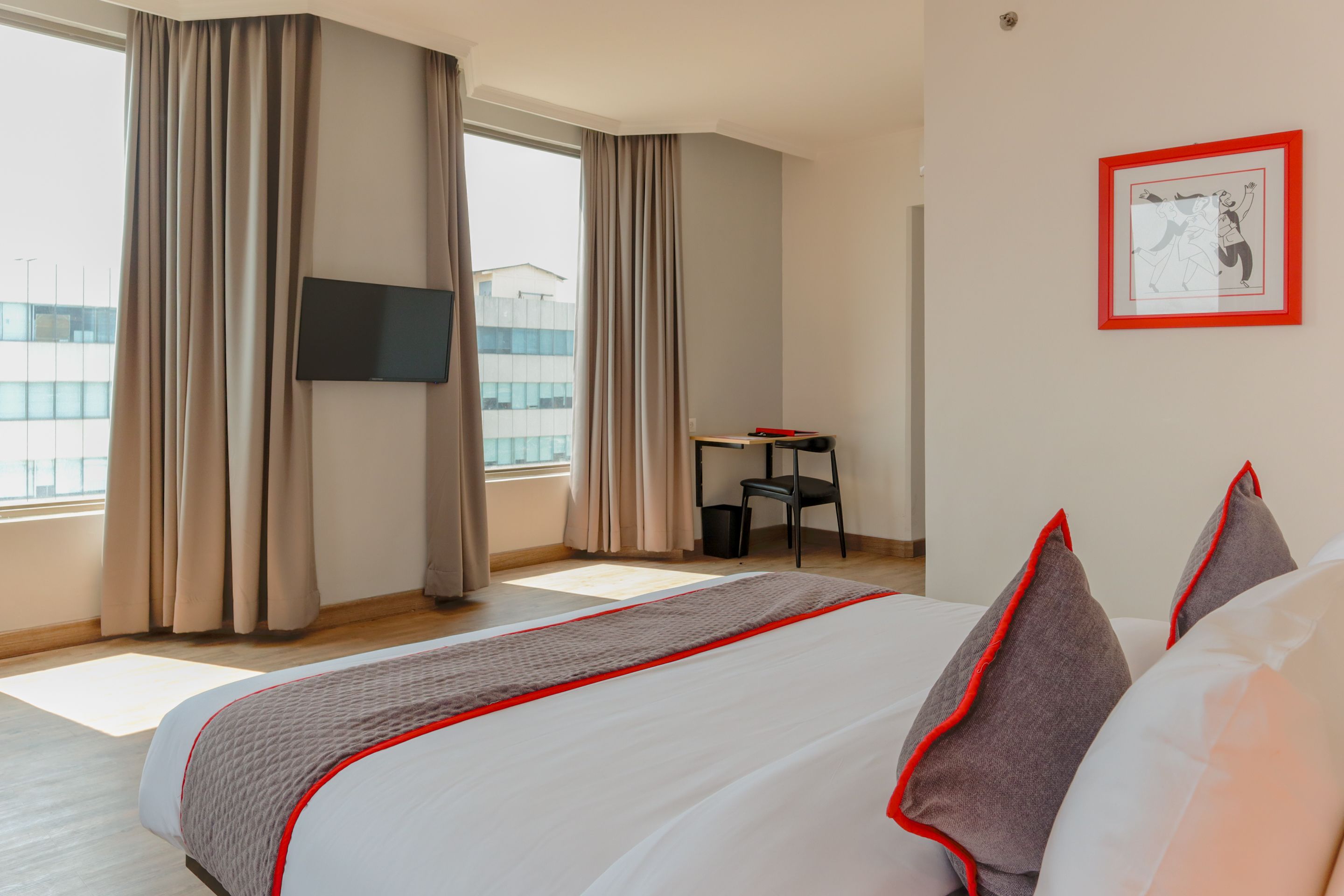 A hotel room with a large bed, a desk, a chair, a TV, and a window with curtains.