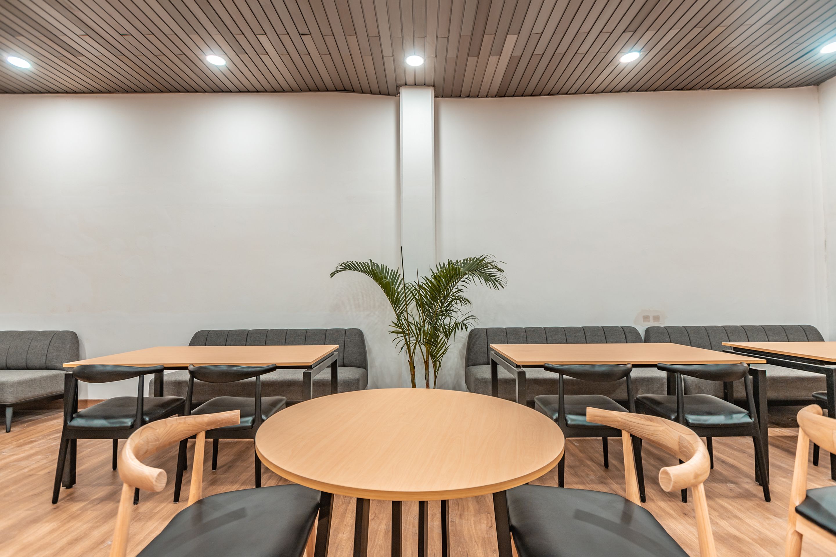 Una sala de reuniones moderna con una mesa redonda, mesas rectangulares y sofás grises.