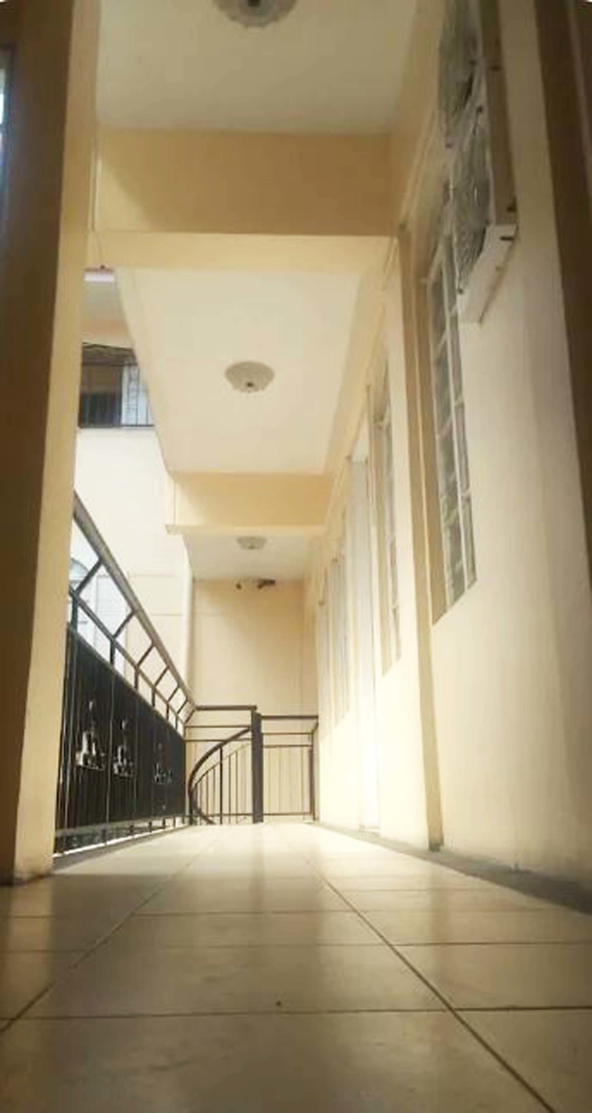 A corridor with tiled flooring, a ceiling with recessed lighting, and a metal railing on one side.