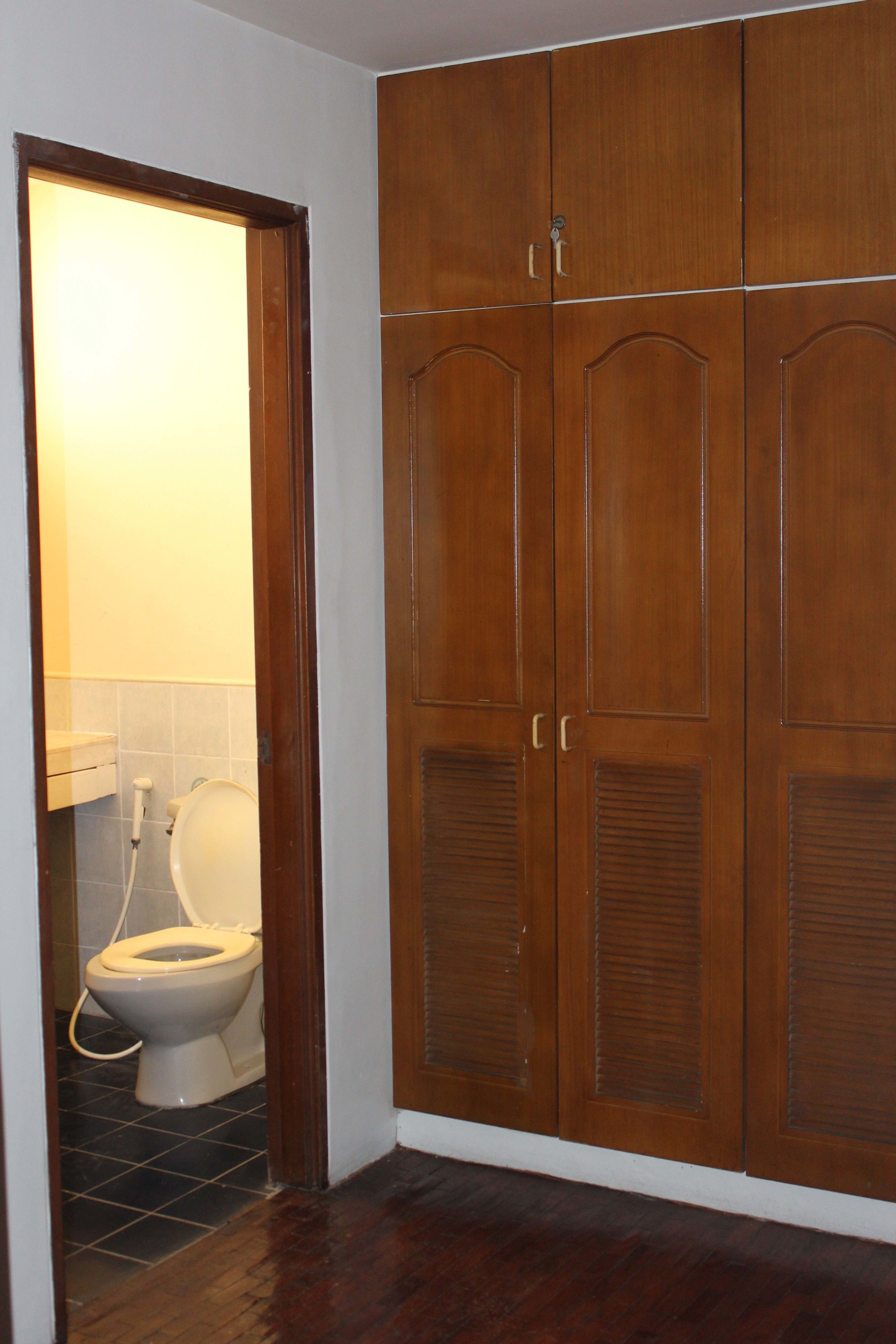 A bathroom with a wooden wardrobe, a toilet, and a tiled floor.