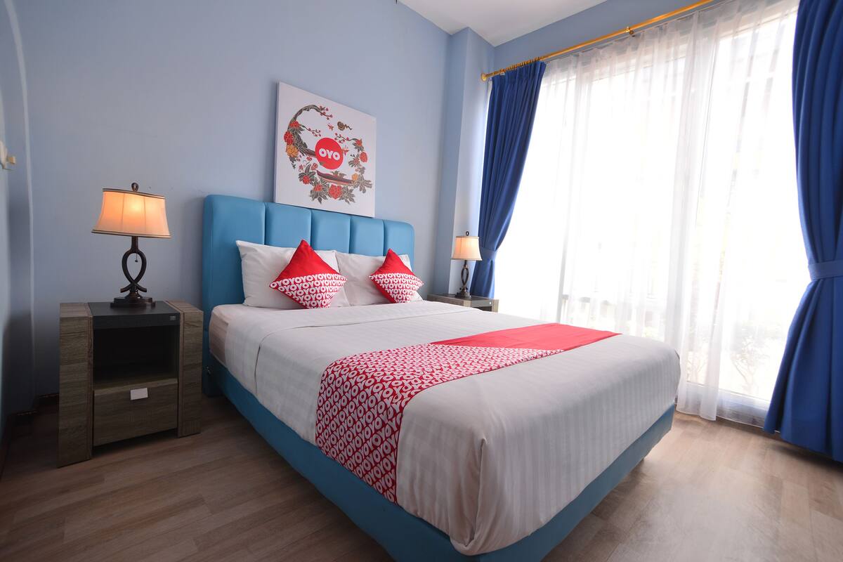 A neatly arranged bedroom with a large bed, a nightstand, a lamp, and a window with curtains.