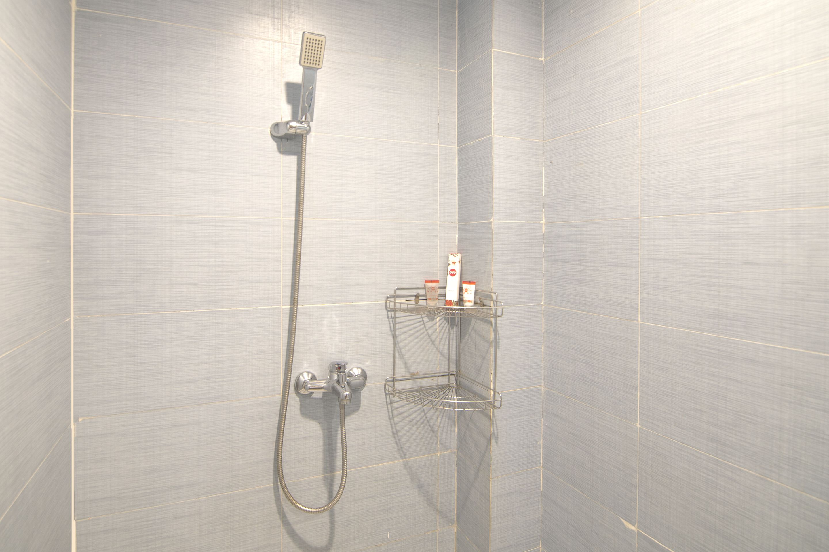 Une douche équipée d’un pommeau de douche à main et d’un robinet mural. Une étagère en métal est prévue pour y déposer les articles de toilette.