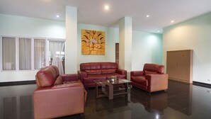 Ein geräumiges Wohnzimmer mit einer großen braunen Ledersofa, einem kleineren braunen Ledersessel und einem Glastisch. Ein großes Fenster mit weißen Vorhängen, eine Holzkommode und ein an der Wand befestigtes Kunstwerk sind ebenfalls zu sehen.