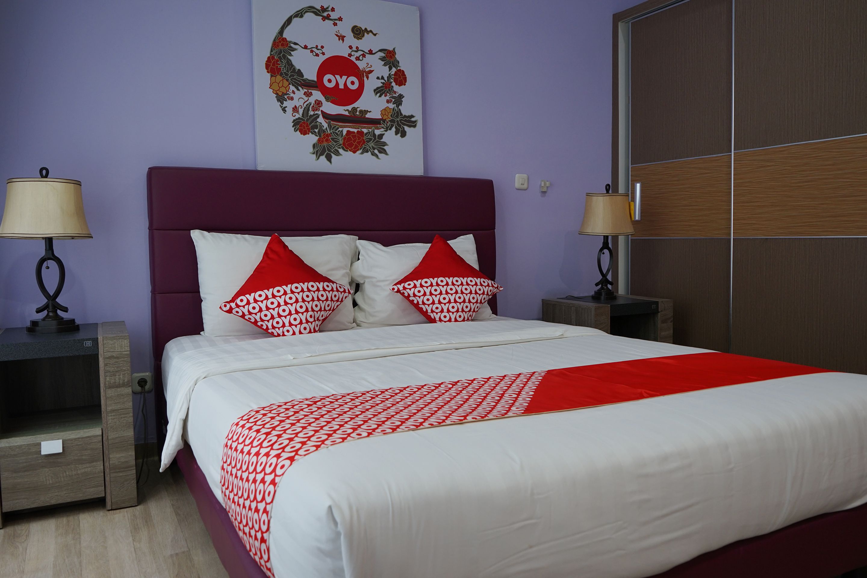 A neatly made bed with a white and red patterned bedspread, two red and white pillows, and a headboard with a floral design.