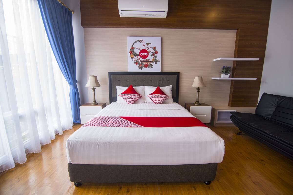 A neatly arranged bedroom with a large bed, two bedside tables, a wall-mounted air conditioner, and a black sofa.