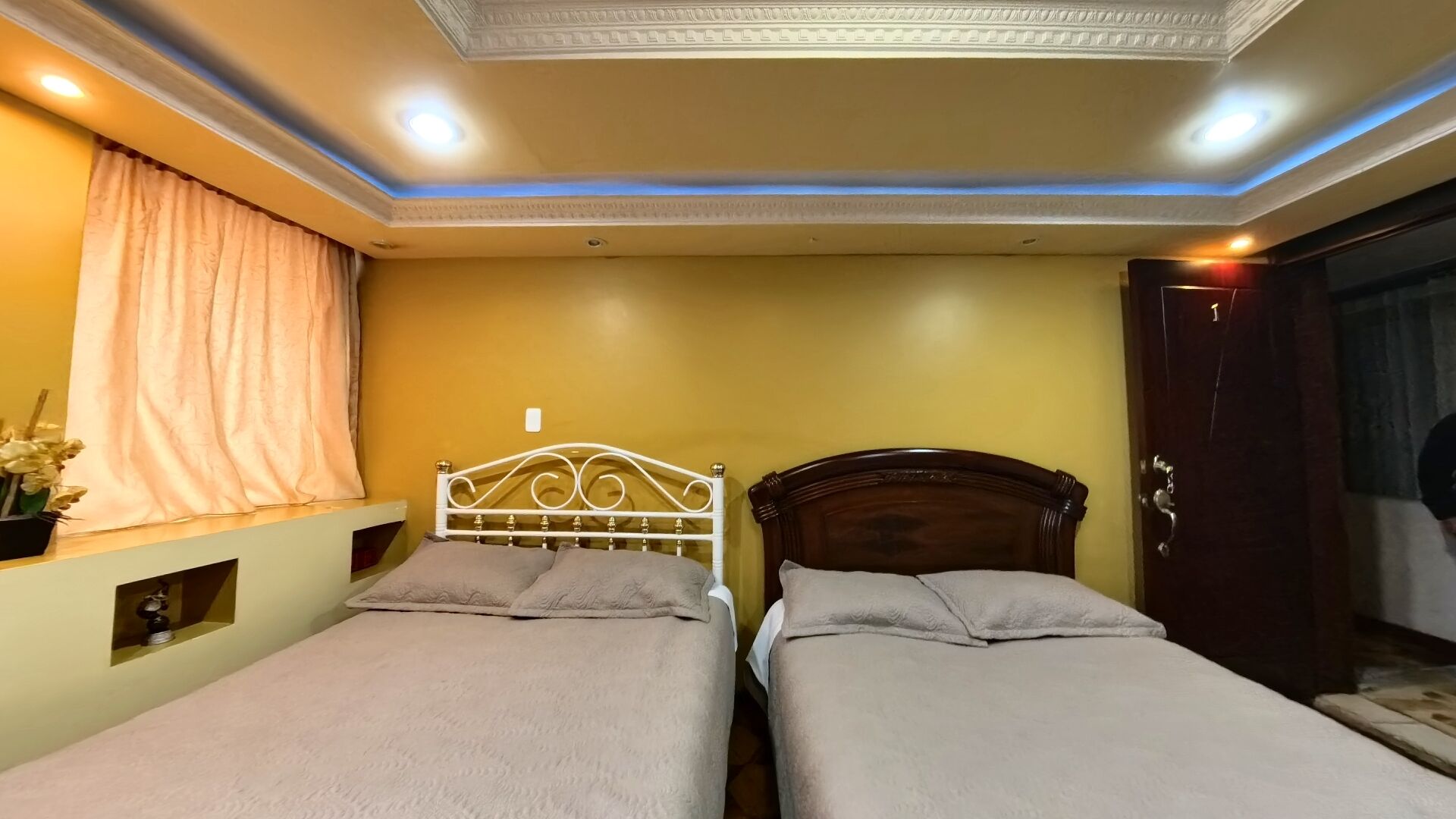 Habitación de hotel con dos camas individuales, techo con iluminación empotrada y ventana con cortinas.