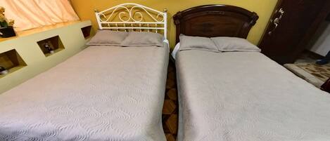 Two single beds with wooden frames, a small shelf with decorative items, and a door to the right.