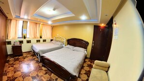 Habitación de hotel con dos camas, piso de madera, ventana con cortinas y puerta con un número.