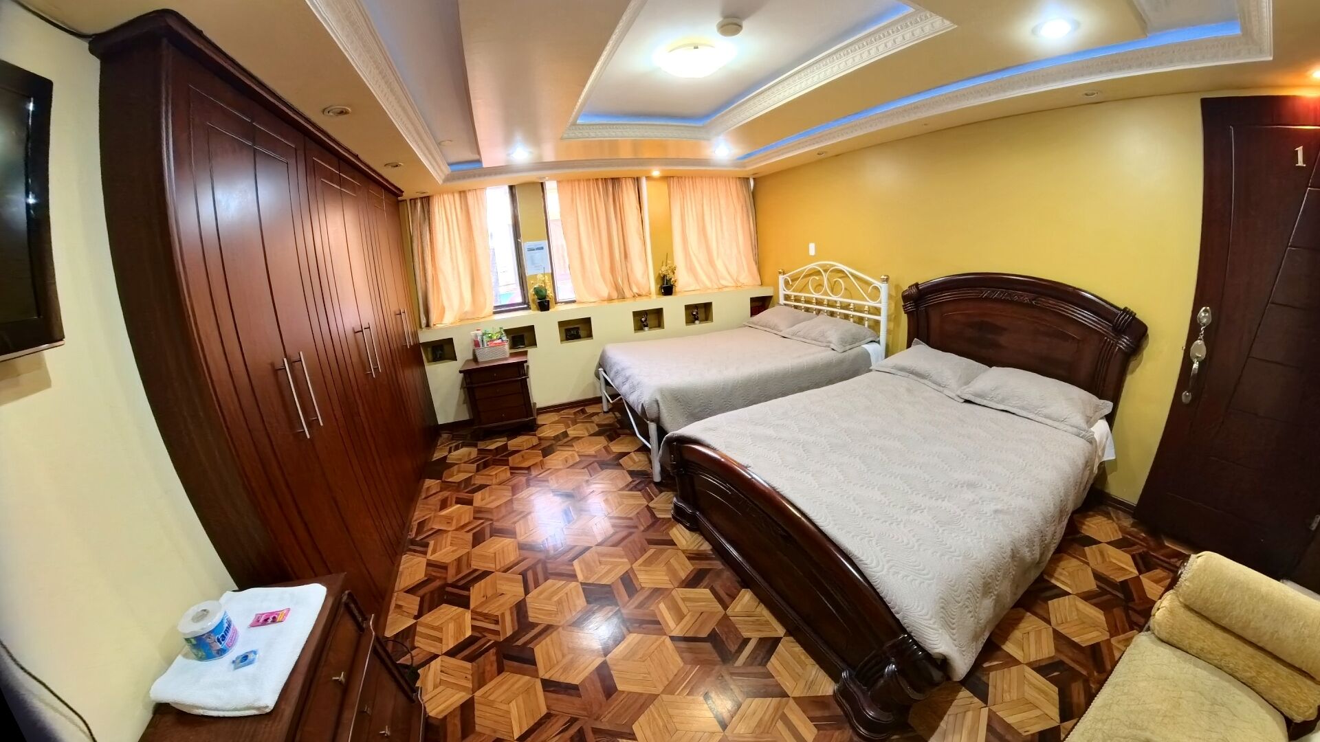 Una habitación de hotel con dos camas, un armario, una tocador con espejo y una ventana con cortinas.