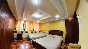 Habitación de hotel con dos camas, un armario de madera, una tocador con espejo e iluminación empotrada en el techo.