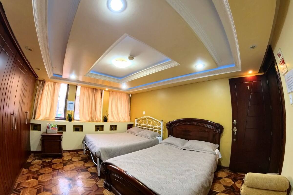Habitación de hotel con dos camas, un armario de madera, una tocador con espejo e iluminación empotrada en el techo.