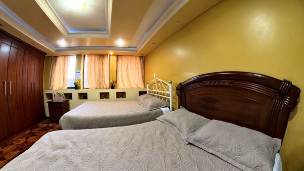 Una habitación con dos camas, un armario de madera, una ventana con cortinas e iluminación empotrada en el techo.