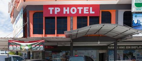 Un hotel con un llamativo letrero rojo, un acceso cubierto y varios vehículos estacionados.