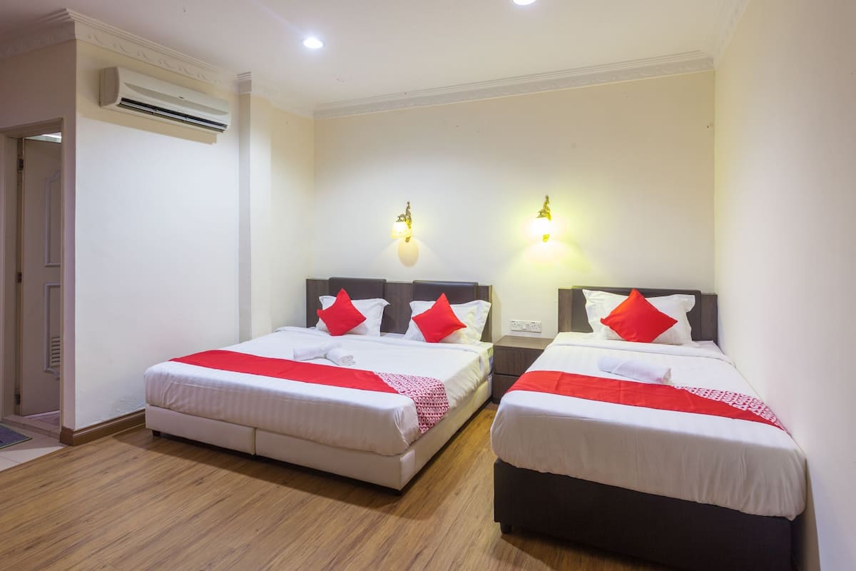 Una habitación de hotel con dos camas, cada una con ropa blanca y almohadas rojas, suelo de madera y una lámpara en el techo.