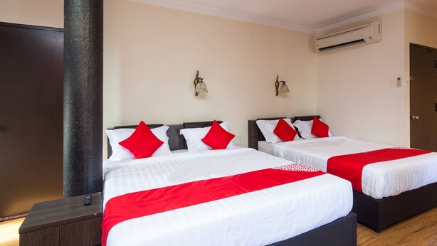 Een hotelkamer met twee bedden, elk met witte lakens en rode kussens, een houten nachtkastje, een grote zuil en een airconditioner aan de muur.