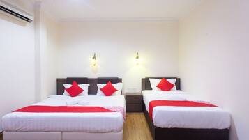 A hotel room with two single beds, each with a wooden headboard, white bedding, and red pillows. There are two wall-mounted light fixtures and a ceiling light.