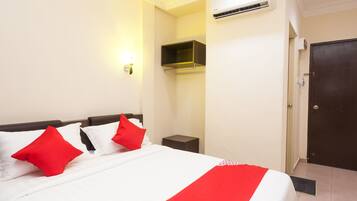 A hotel room with a bed, a nightstand, an air conditioning unit, a wall-mounted shelf, and a door.