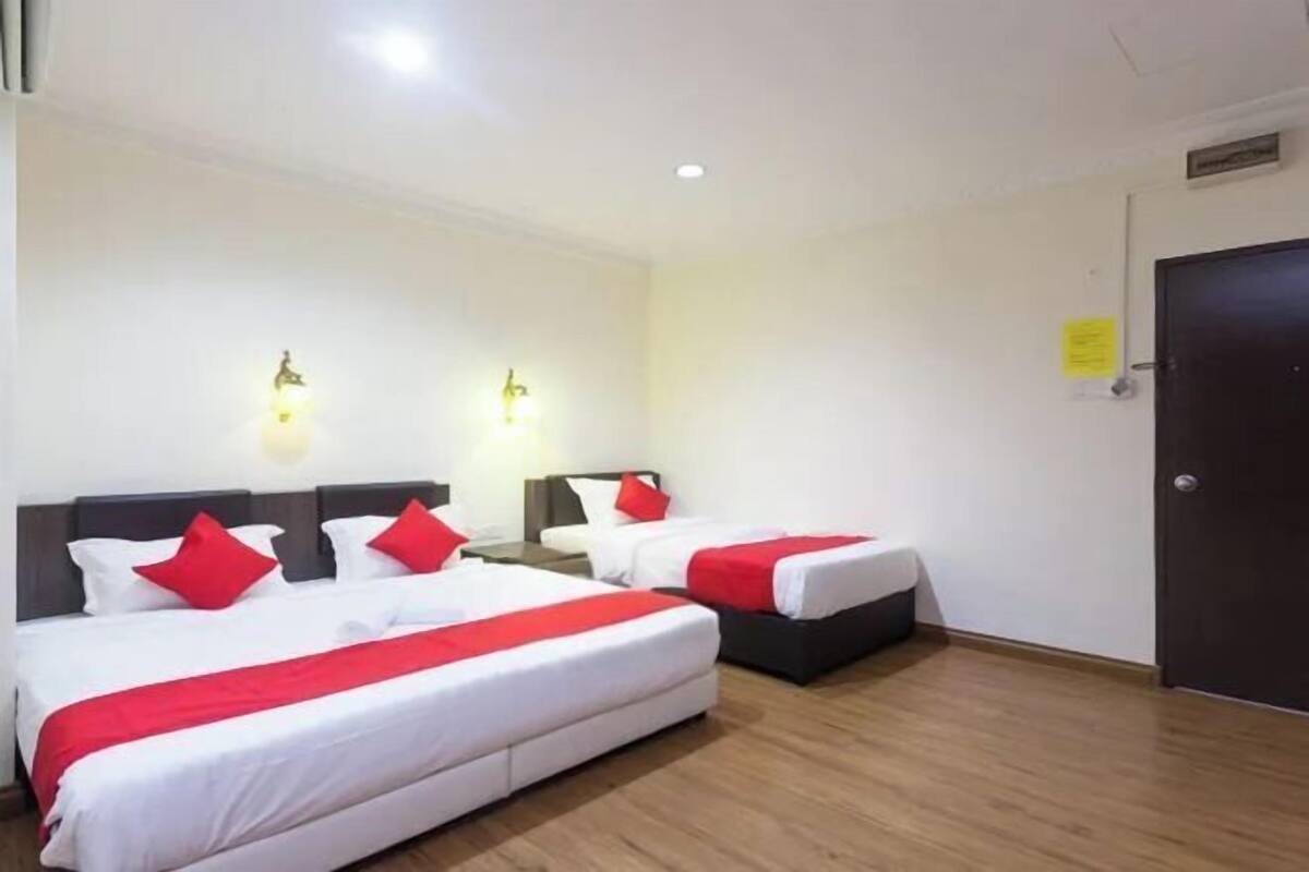 Habitación de hotel con dos camas, cada una con ropa de cama blanca y almohadas rojas, piso de madera y una puerta a la derecha.