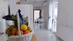 Eine Küche mit Obstkorb auf der Arbeitsfläche, einem Essbereich mit Tisch und Stühlen sowie einem Blick ins Freie durch ein Fenster.
