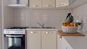Eine Küche mit Gasherd, Backofen und Spüle. Auf der Arbeitsplatte steht ein Obstkorb.