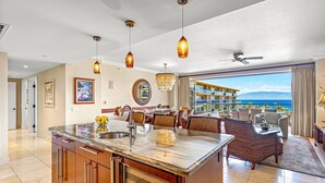 A spacious kitchen with a marble island, modern pendant lights, and a view of the ocean. - Maui Resort Rentals: Honua Kai Konea 625 - 6th Floor 3BR w/ Ocean Views from Every Room! (Lahaina)