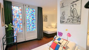 Una habitación con cama, mesita de noche, un jarrón con flores y un cuadro en la pared.